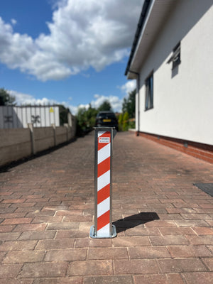 Bollard with red and white stripes on a paved driveway next to a house.