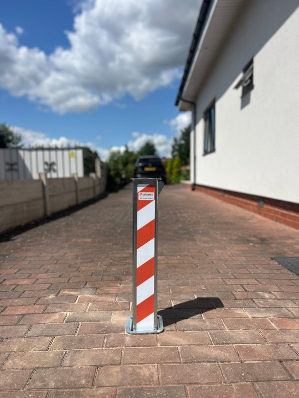Bollard with red and white stripes on a paved driveway next to a house.